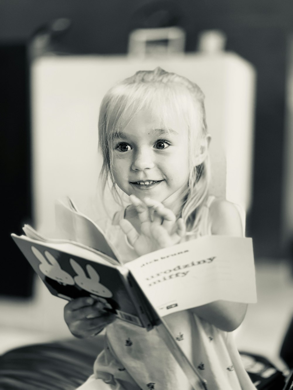 grayscale photo of girl holding book and smiling