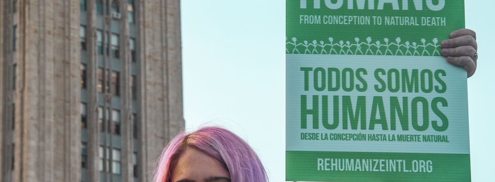 woman with pink hair holding green placard