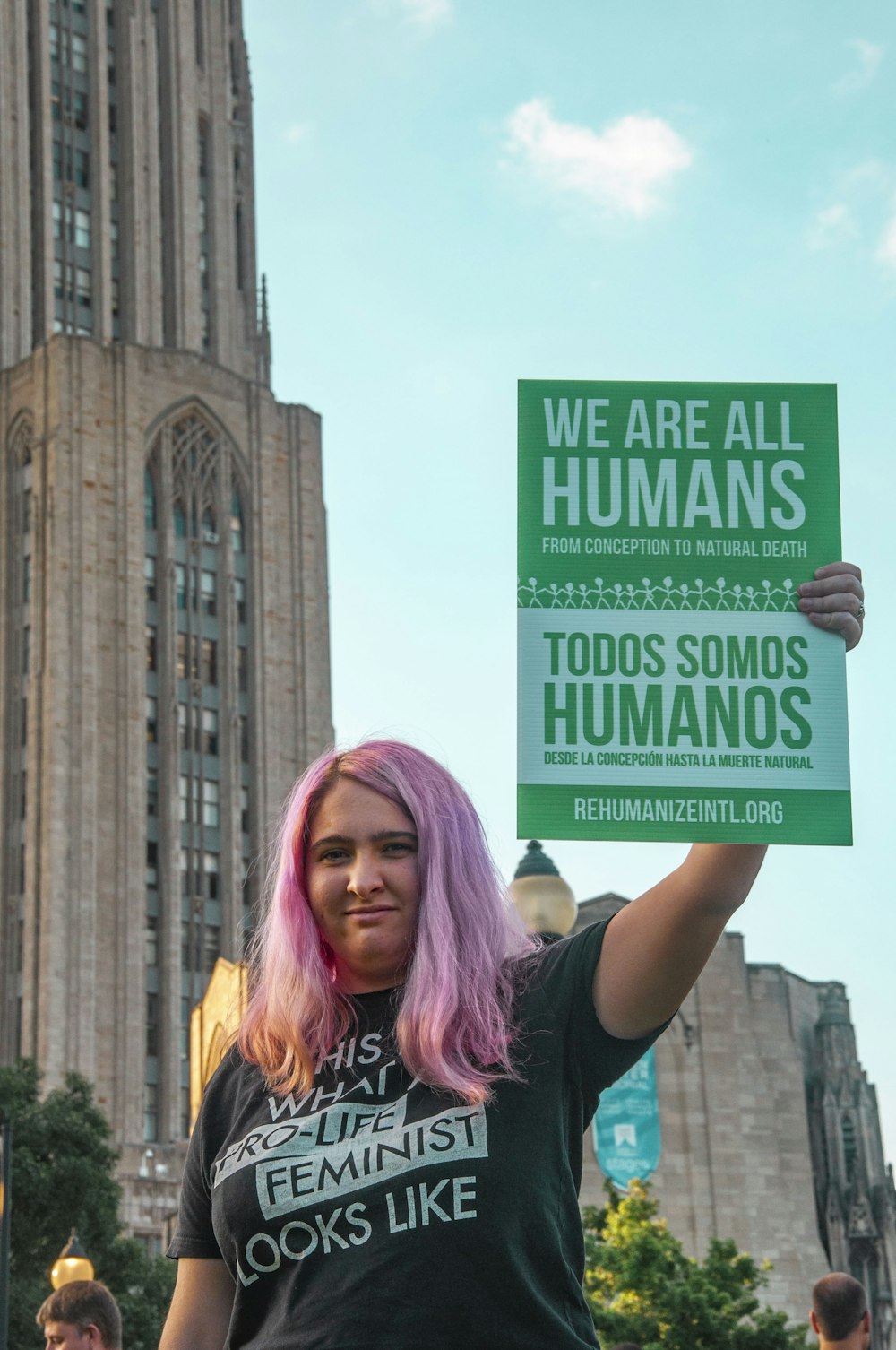 woman with pink hair holding green placard