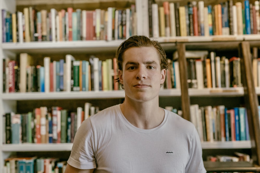 man wearing white shirt standing beside bookcase