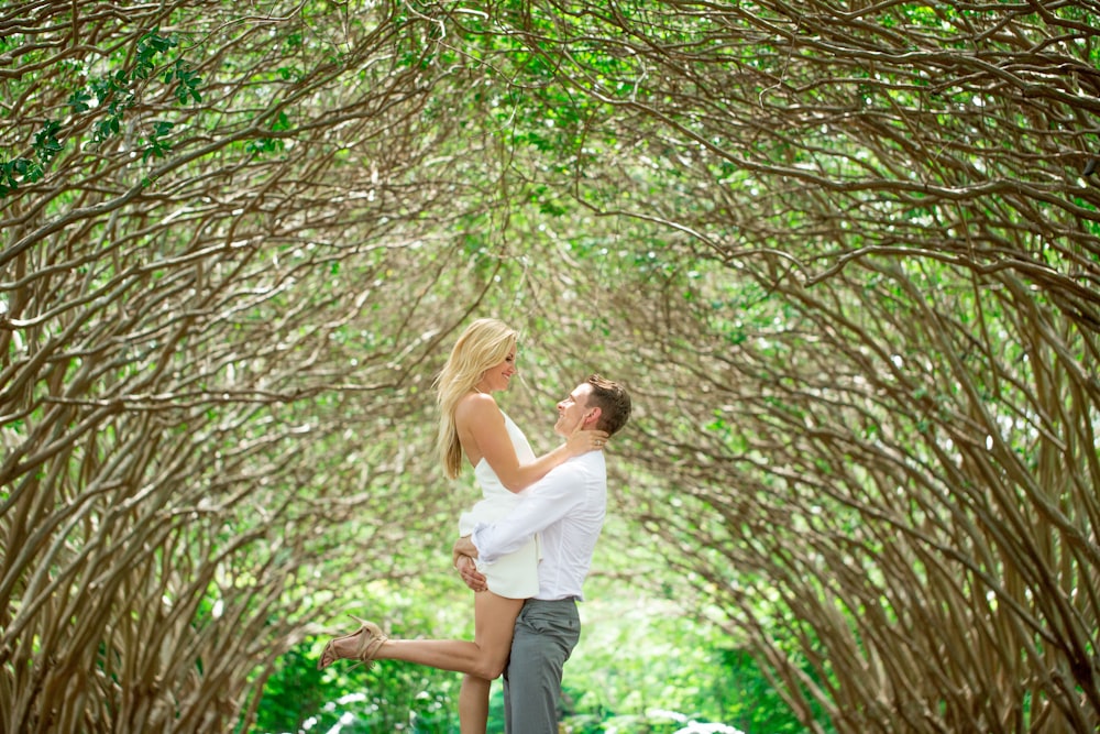 man lifting woman under green-leafed trees