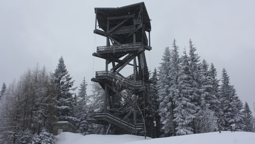 a snow covered forest with a tall structure in the middle of it