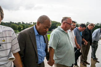 A group of men sharing a moment of prayer and encouragement outdoors at sunrise.