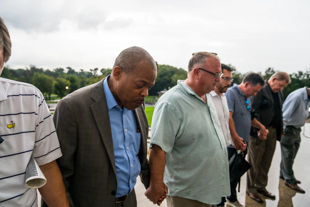A group of men gathered outdoors in fellowship, sharing a moment of prayer and encouragement.