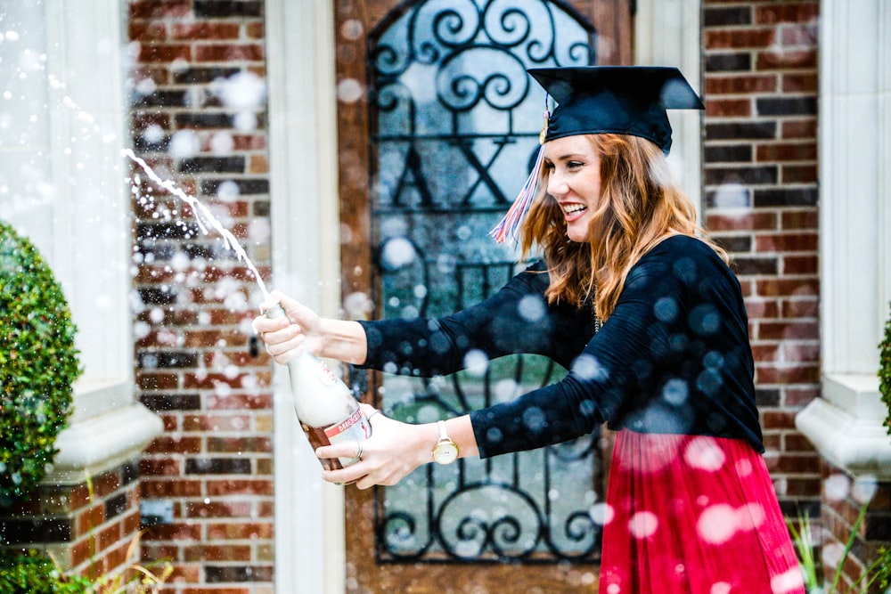 woman in black long-sleeved blazer wearing graduation cap holding wine bottle