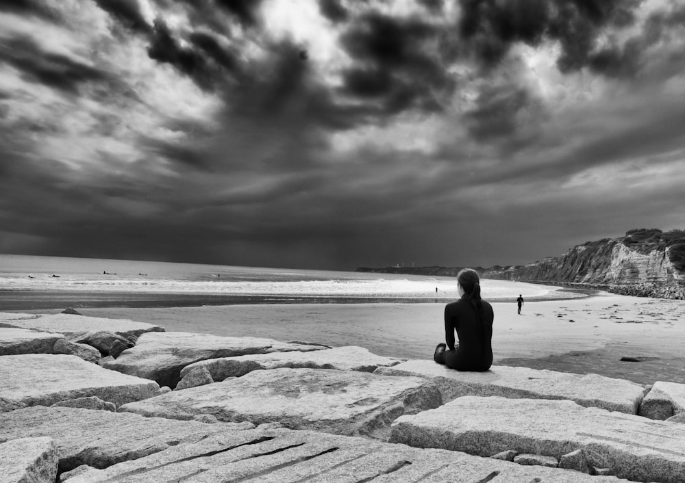 grayscale photo of person sitting in near ocean during daytime