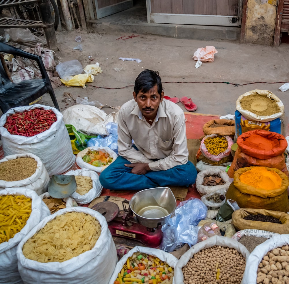 Homme assis sur une natte rouge entouré de condiments