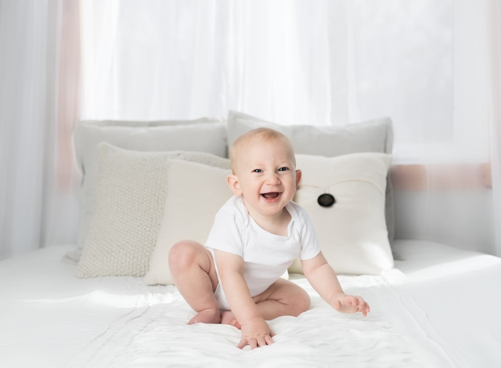 smiling baby sitting on white bed