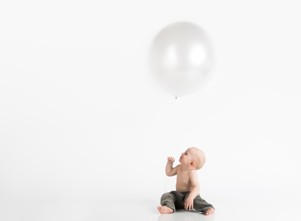 boy sitting wearing black pants under white balloon