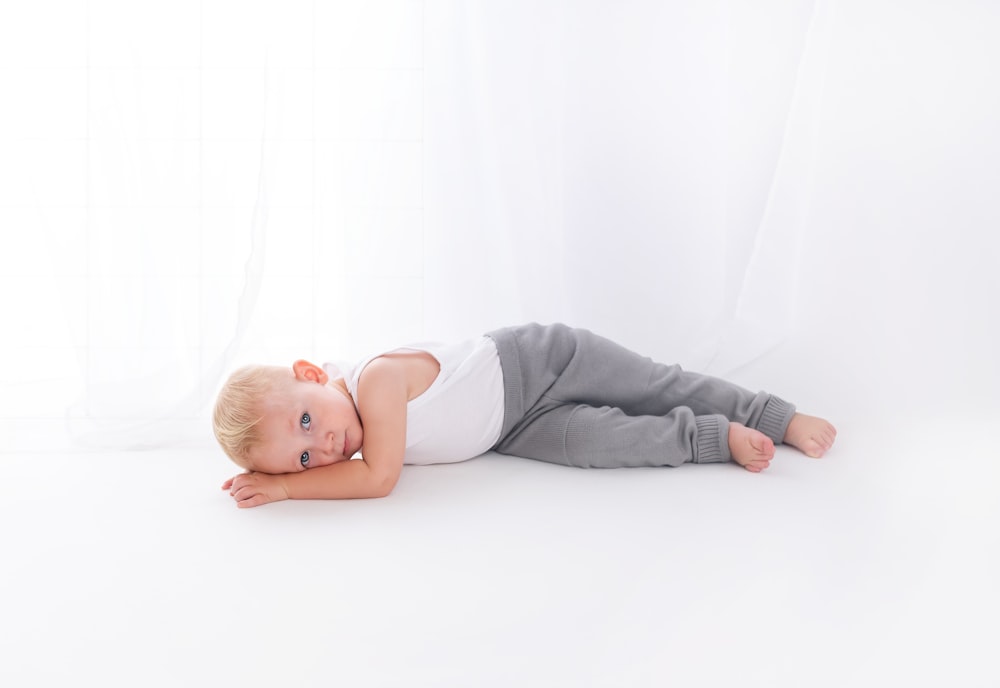 boy wearing white tank top lying on white surface close-up photography