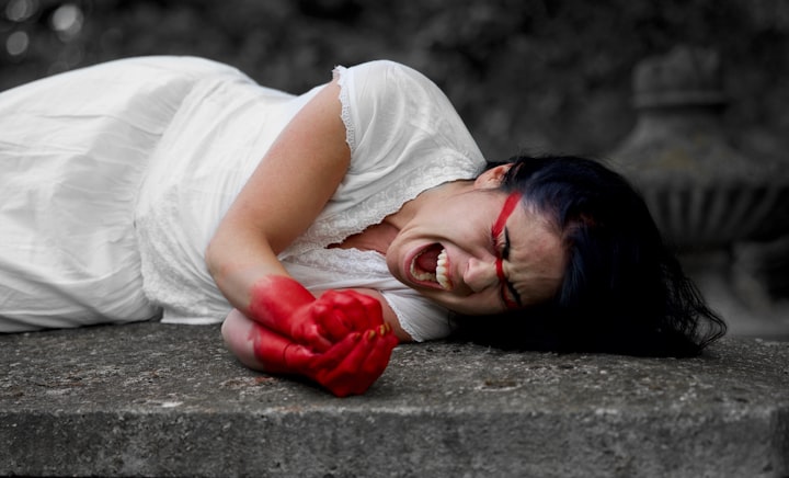 A woman with red paint on her hands and across her face on the ground crying