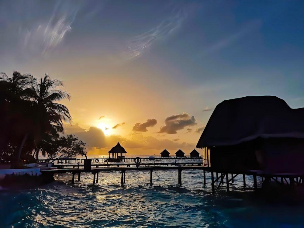 silhouette of nipa huts and palm trees over body of water during golden hour