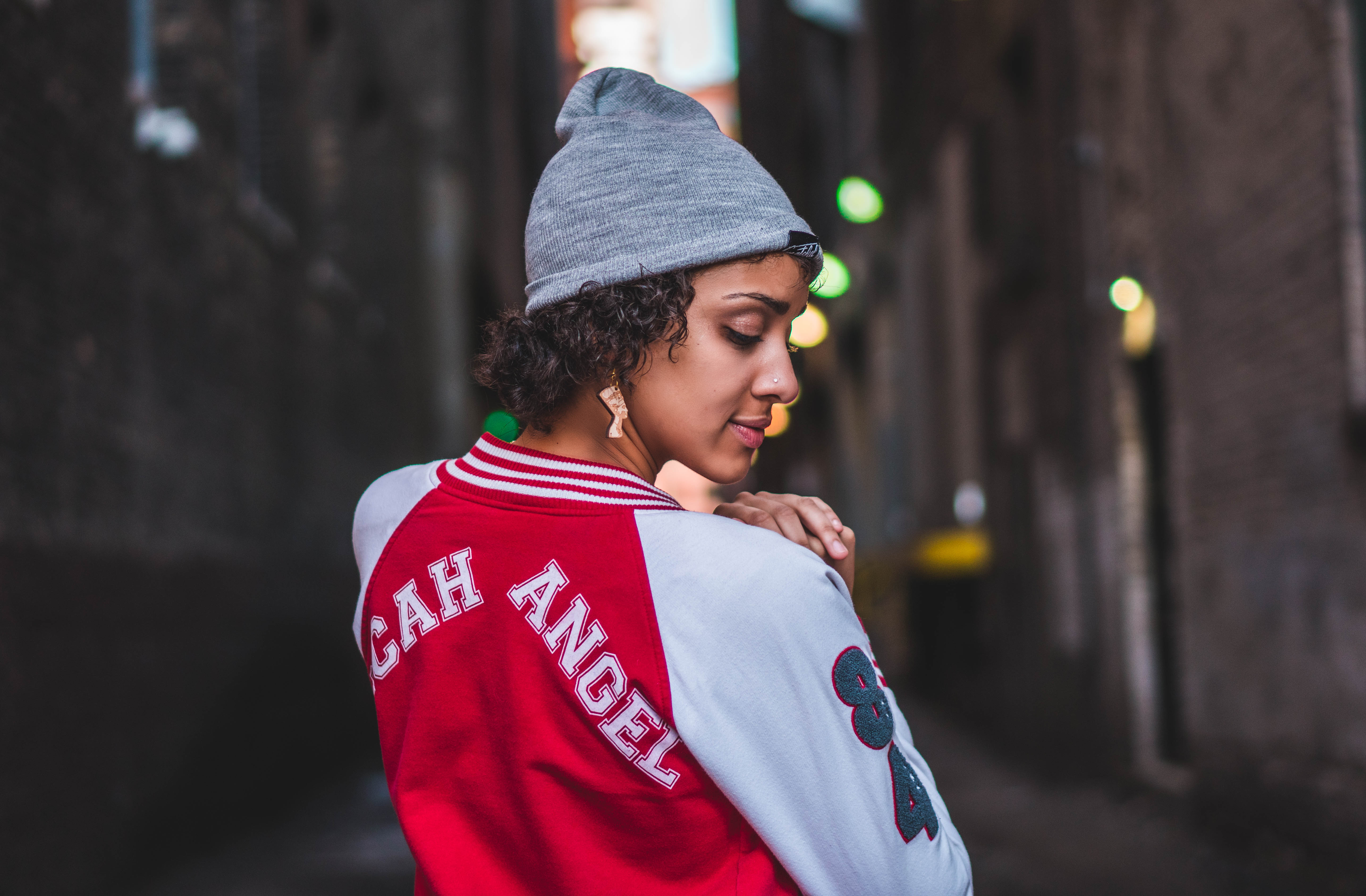 woman wearing red and white jacket and gray knit cap standing while glancing her right side
