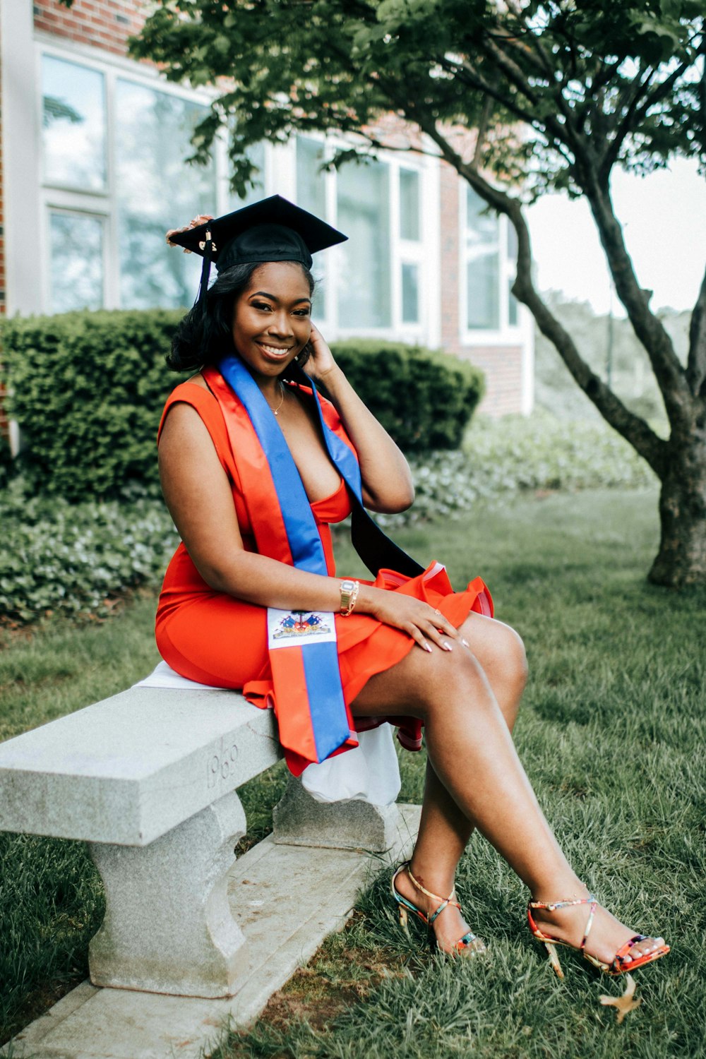 woman with academic hat sits on bench outside the school