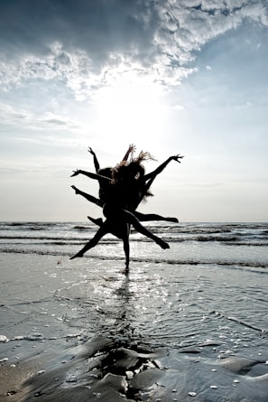 Dancers moving energetically on the sandy beach under a pink and blue sunset sky.