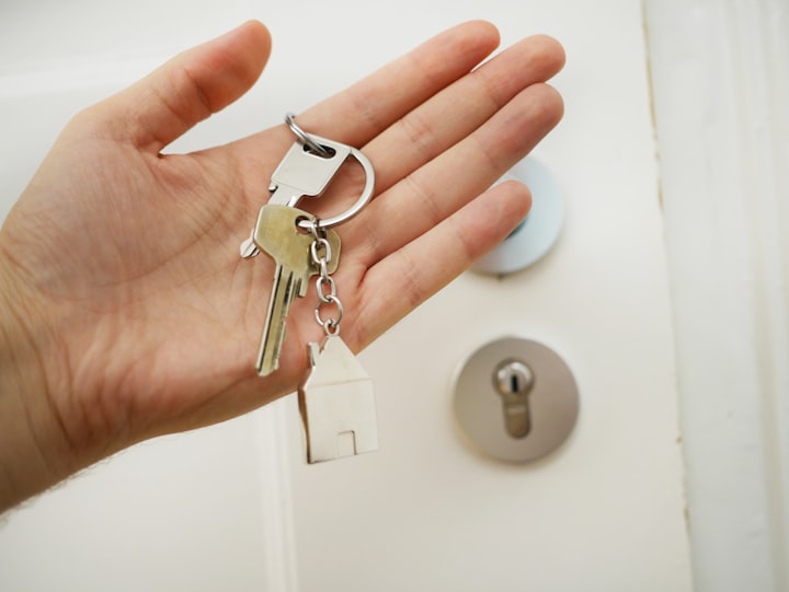 person holding a set of keys in their hands with a little house key chain in front of their new home's door