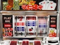A close-up view of a slot machine with vibrant colors and various gambling symbols such as dice, coins, and playing cards. The reels display a combination of symbols, including bars, cherries, and the number seven. The chrome exterior and colorful details convey the theme of casino and gambling.
