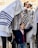 A group of people engage in a religious ceremony, with a young boy looking upward, standing partially under a prayer shawl held by someone. The atmosphere is busy with multiple participants wearing traditional attire, and some men have phylacteries on their heads. The setting appears to be a holy site.