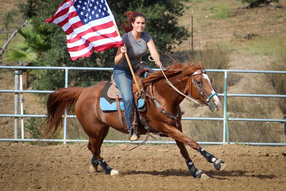 낮 동안 갈색 말을 타고 미국 국기를 들고 있는 여자
