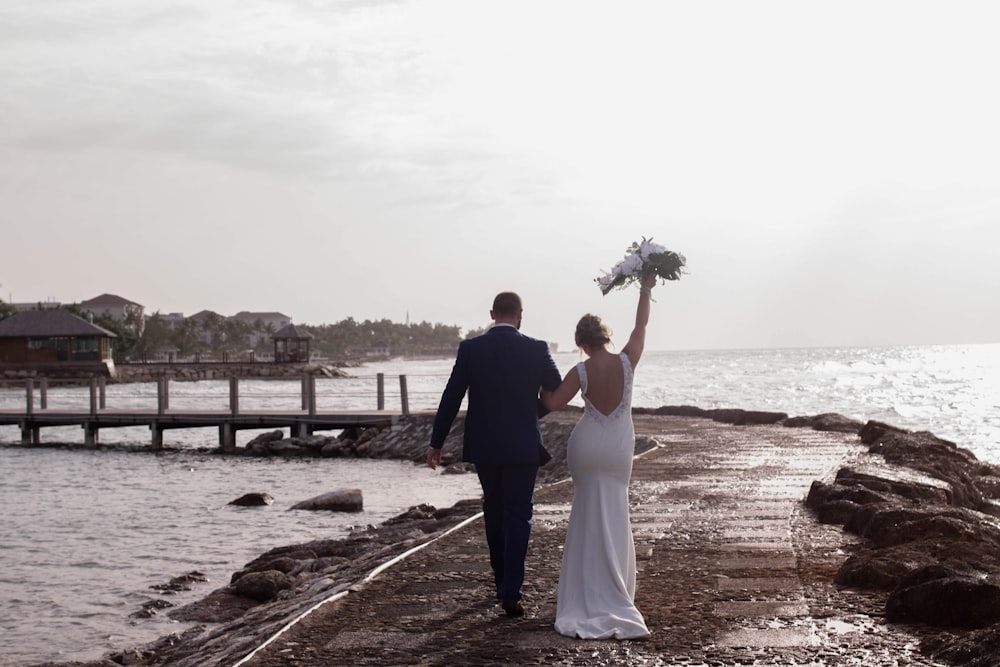 a bride and groom walking along a pier towards the ocean