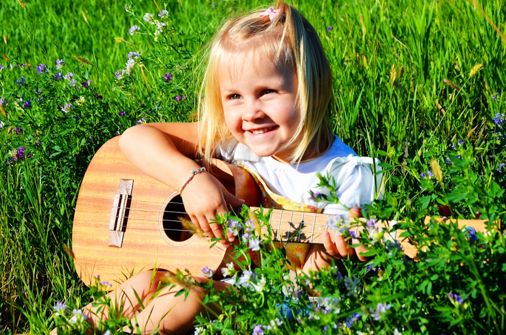 a little girl sitting in the grass playing a guitar