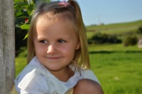 Smiling little girl wearing a bright pink bow in her hair outdoors on a sunny day.