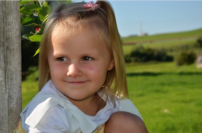 Smiling little girl wearing a bright pink bow in her hair outdoors on a sunny day.