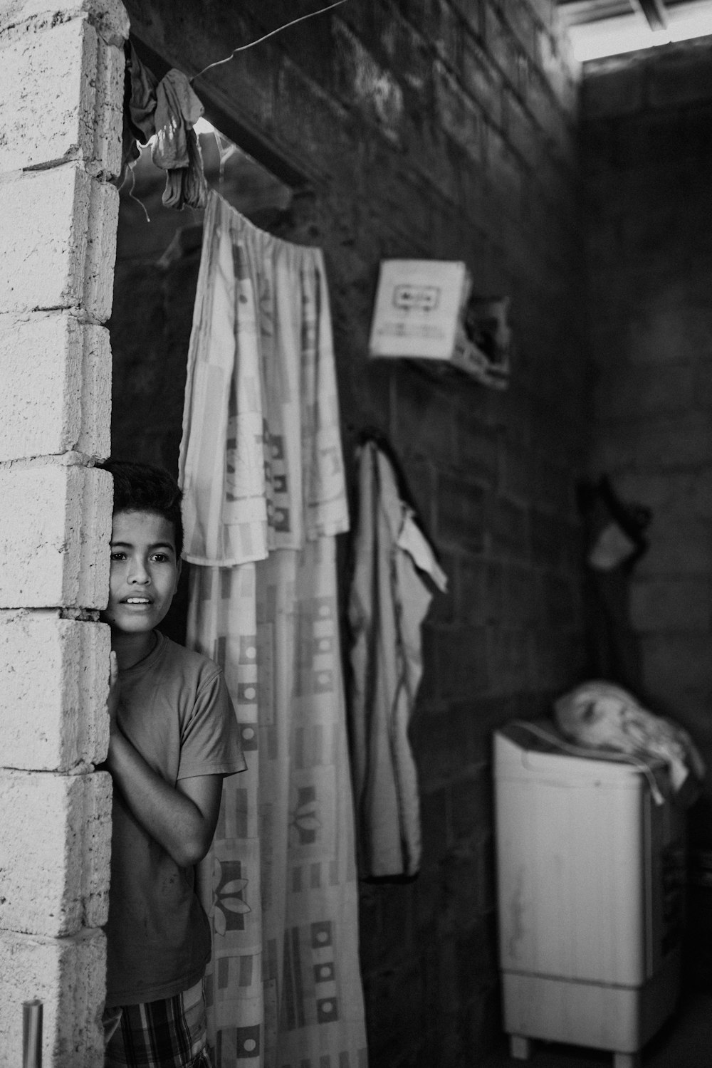 a black and white photo of a boy peeking out of a window