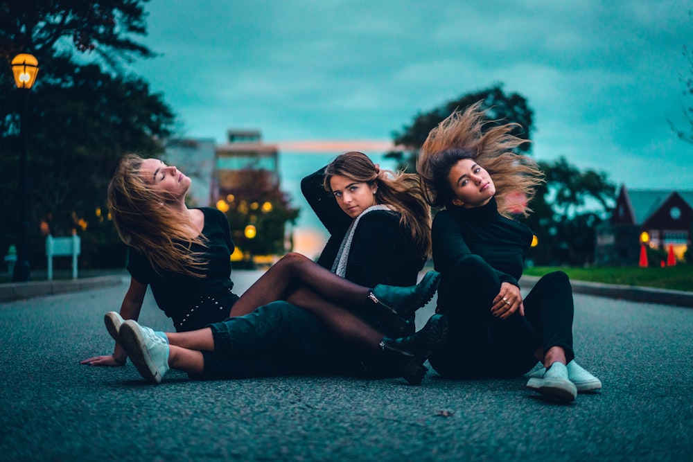 three women sitting on asphalt road