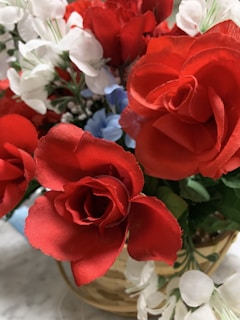 A bouquet of vibrant red roses surrounded by white flowers and hints of blue, set in a woven basket. The arrangement is lush and full, with green leaves adding depth.