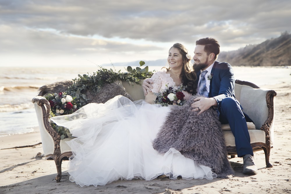 man and woman sitting on padded sofa beside sea