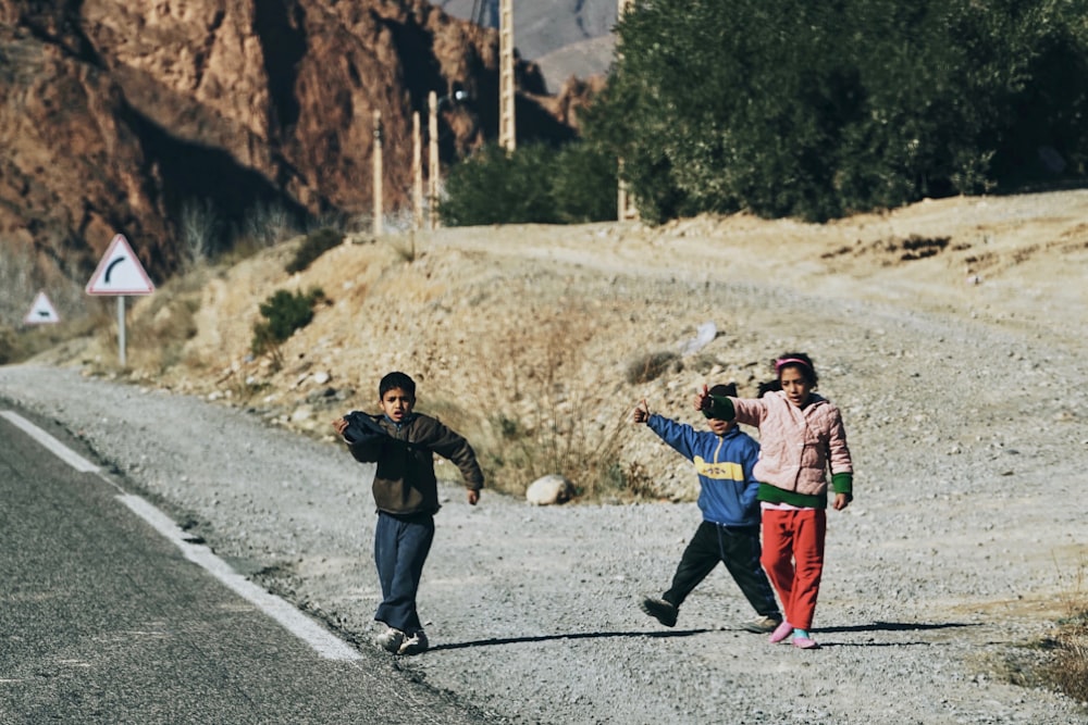 three kids walking on gray ground beside road