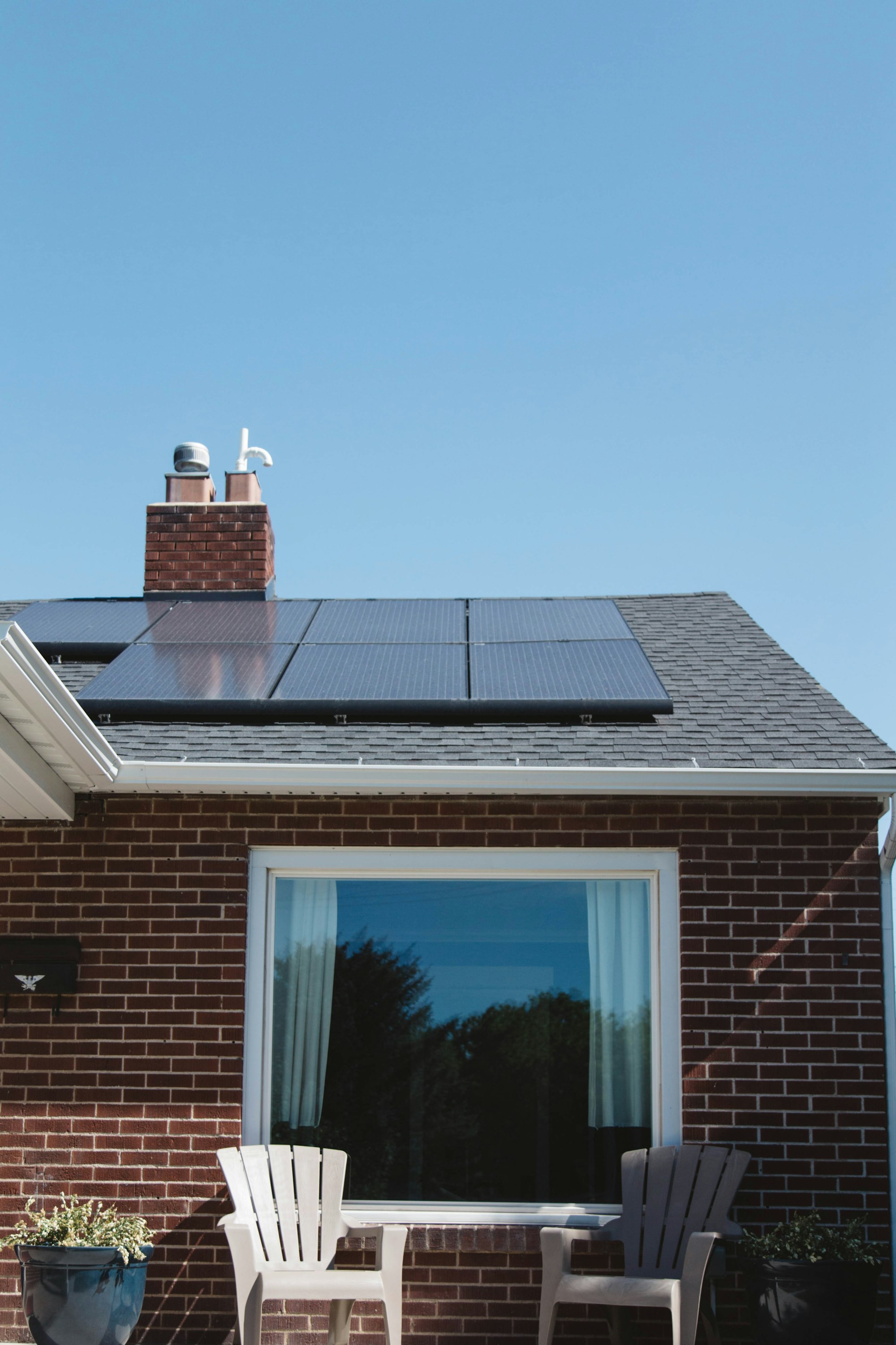 Vivint Solar - Solar Panels on roof of brick home with window and Adirondack chairs. 