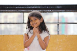 A young girl repeating English phrases aloud with a smile in her bedroom.