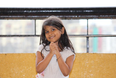 A young girl repeating English phrases aloud with a smile in her bedroom.