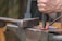 A hand is holding a chisel and hammering a red-hot piece of metal on an anvil, illustrating metalworking in progress.