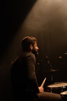 Drummer mid-beat, sweat flying, surrounded by vintage drum kit under moody stage lights.