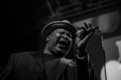Close-up of the lead singer passionately singing into the microphone, wearing a vintage Britpop style jacket.