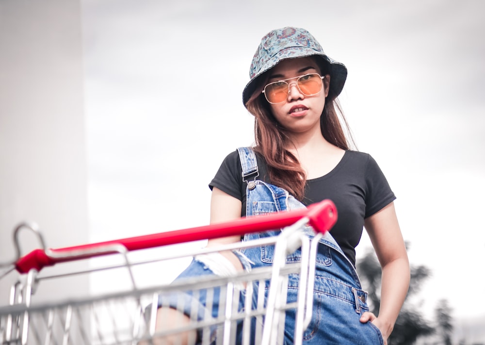 woman stepping on shopping cart wearing blue denim jumpsuit