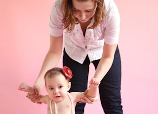 barefooted woman standing and assisting baby while walking