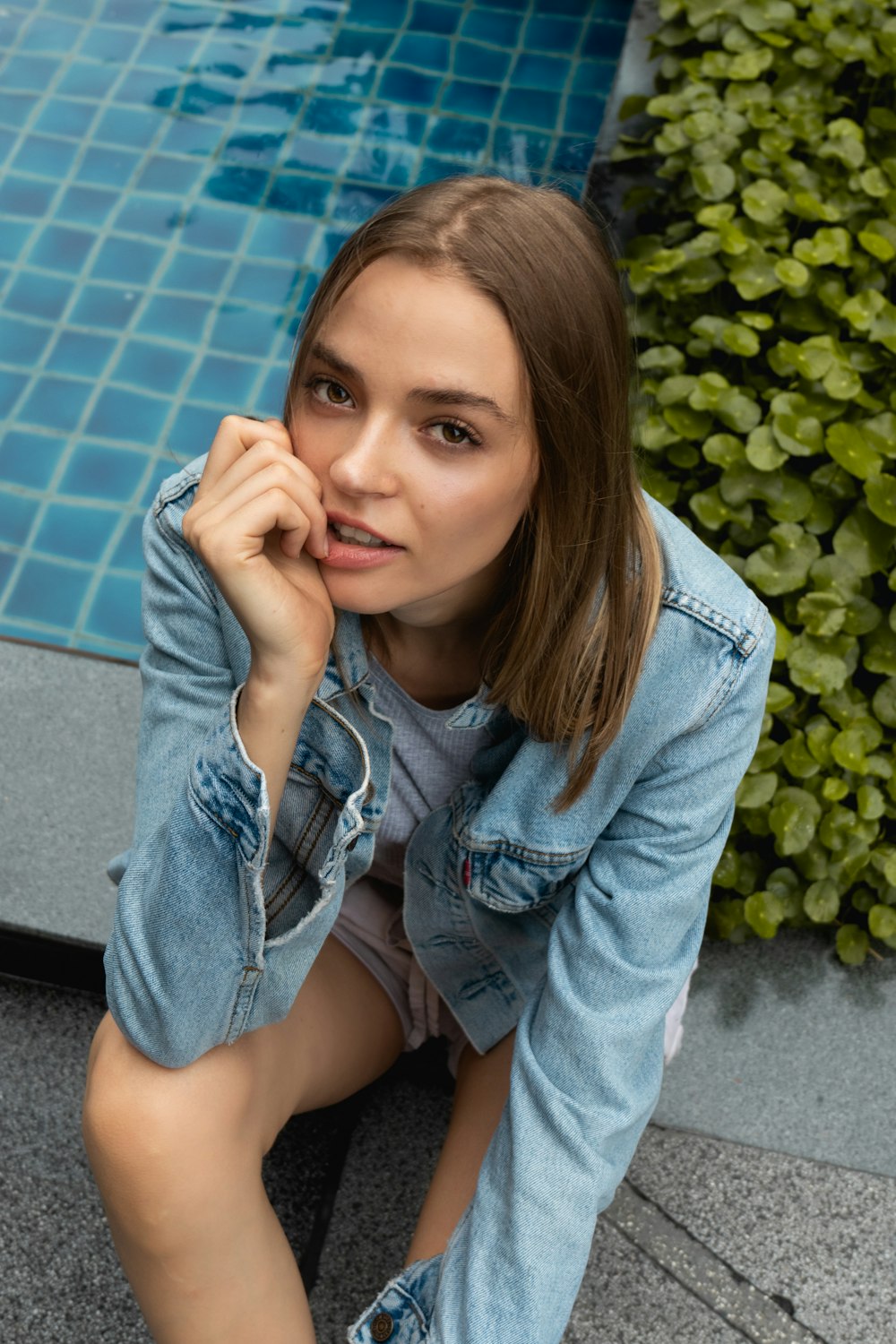 woman wearing blue denim button-up jacket sitting beside pool