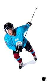 A hockey player in motion is captured on the ice. Dressed in a bright blue jersey, maroon and blue socks, and black gloves, the athlete is focused and poised with a hockey stick ready for action. The background is a clean, stark white, emphasizing the player's dynamic stance and expression.