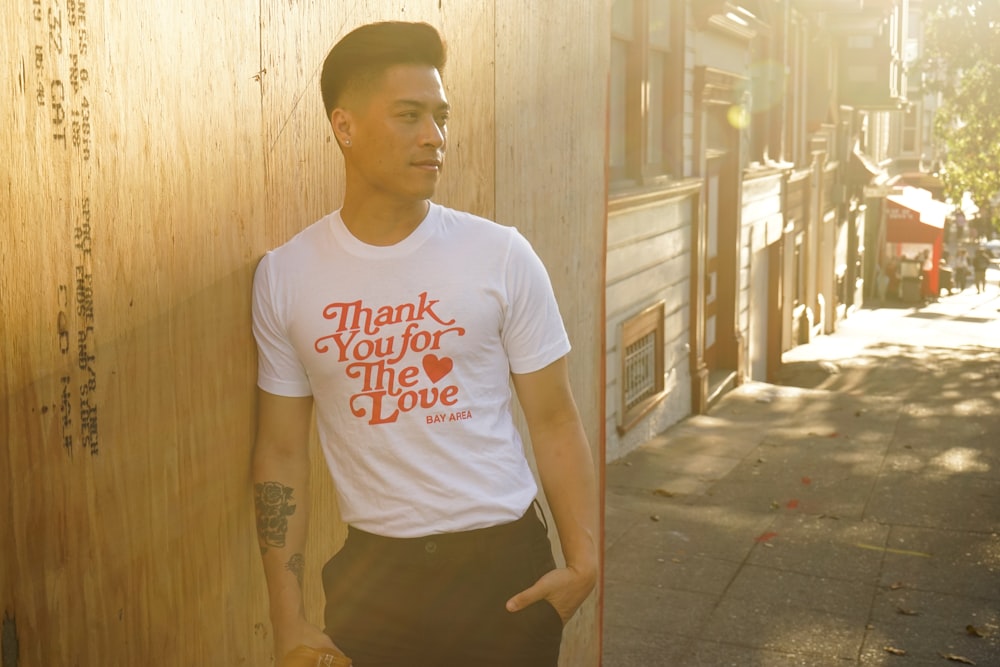 man in white shirt leaning on brown wall during daytime