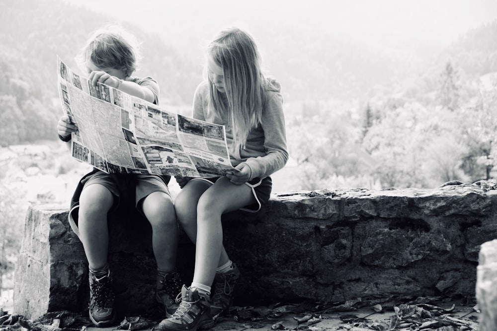grayscale photo of boy and girl reading newspaper