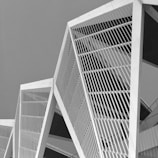 The image features a series of modern architectural structures with geometric lines and patterns. The design is composed of angular forms intersected by parallel lines, creating a stylish and contemporary aesthetic in a monochromatic palette.