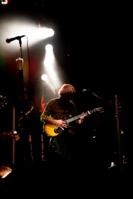 Close-up of a musician playing guitar on stage with dramatic lighting.