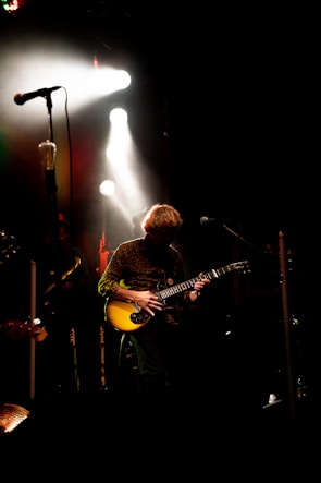 Close-up of a musician passionately playing electric guitar on a dark stage with vibrant spotlights.
