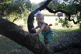 Smiling child wearing a lilare outfit and a matching bow in a sunny park.