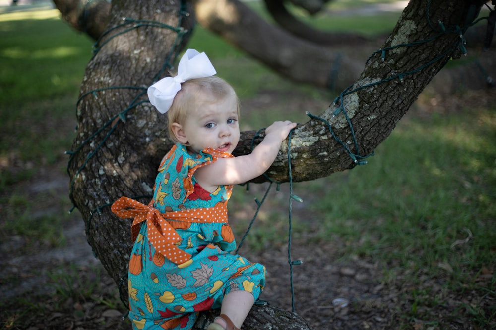 girl in blue, yellow, and orange fruit print sleeveless dress climbing tree