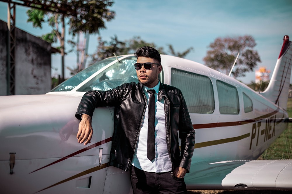 man wearing black leather jacket standing near white airplane